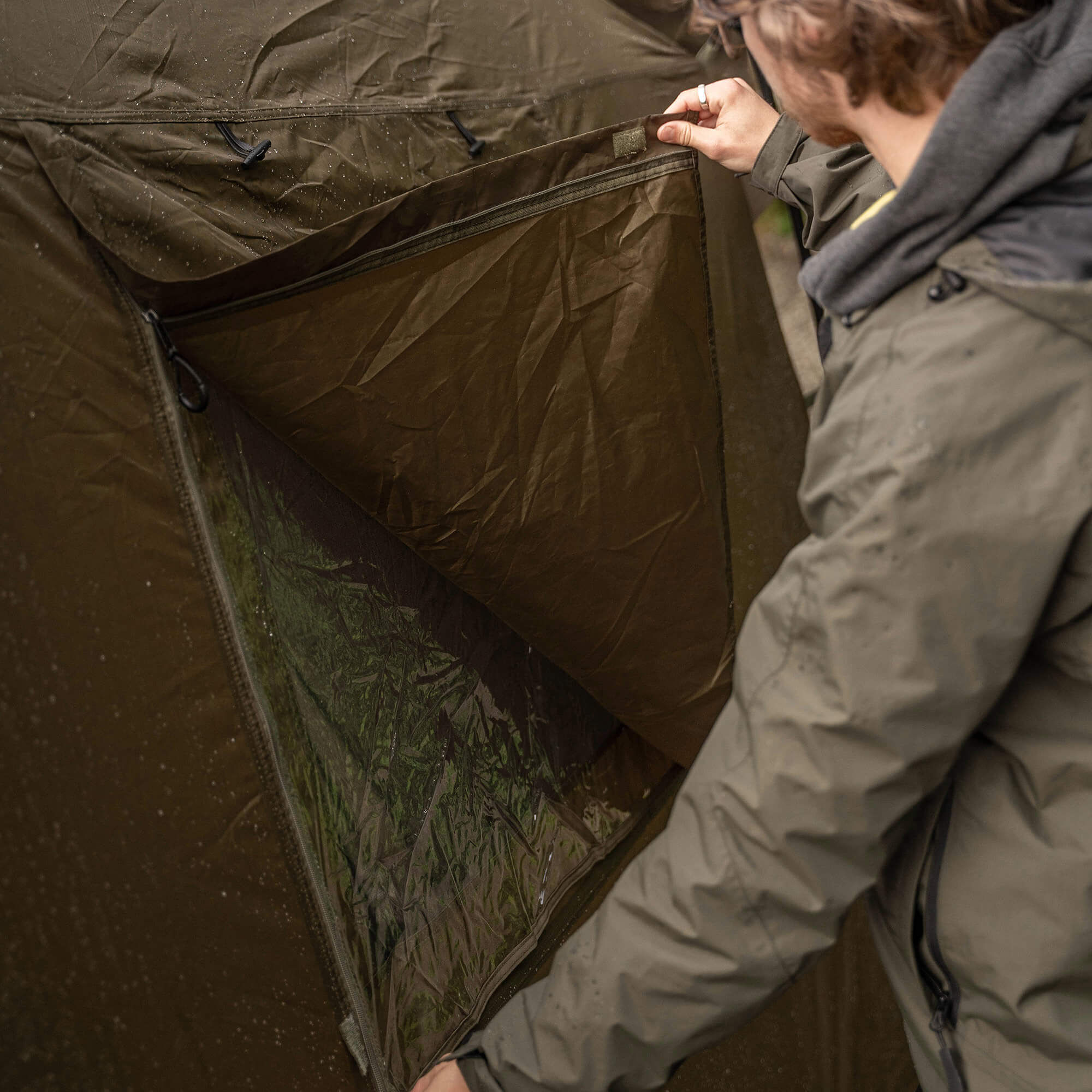 Angler öffnet eine Zeltklappe und ist bereit für ein komfortables Angelerlebnis.