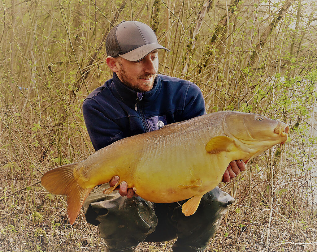 karpfenangeln-mit-boilies Angler hält stolz einen großen Karpfen und präsentiert erfolgreiche Angeltechniken und Angelgeräte.