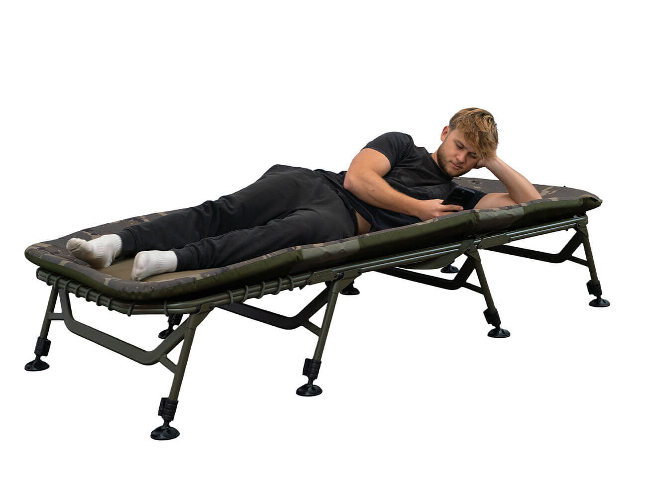 Un pêcheur de carpes se détendant sur un fauteuil-lit de pêche confortable à motif camouflage et doté de pieds réglables.