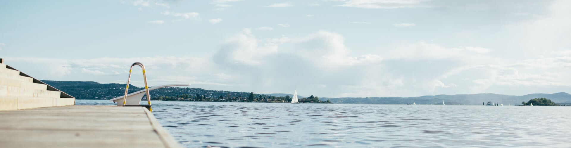 Ein Spungbrett auf eine Steg an einem großen See mit Segelbooten.