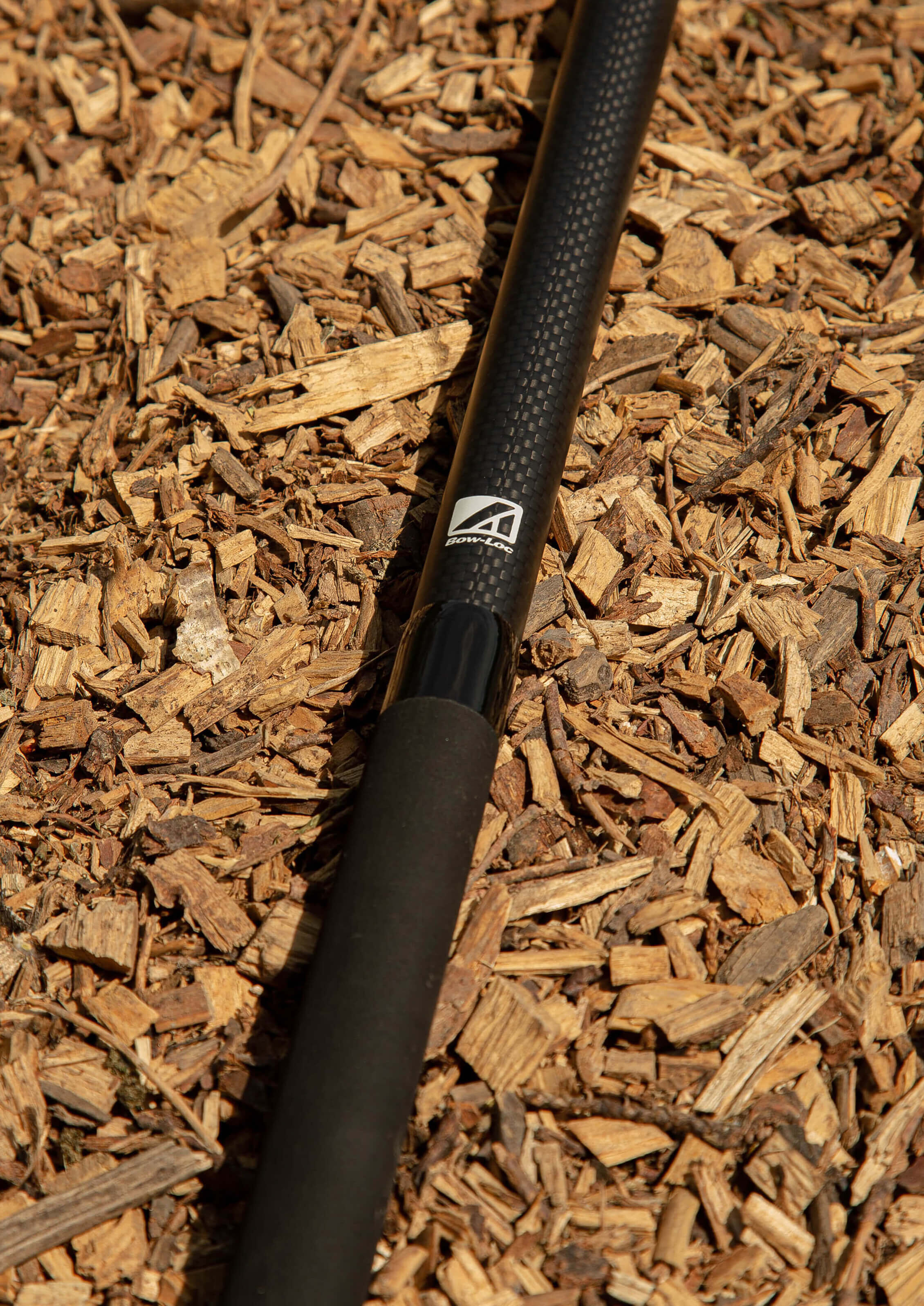 Primo piano di una canna da pesca di alta qualità appoggiata su trucioli di legno, ideale per la pesca alla carpa.
