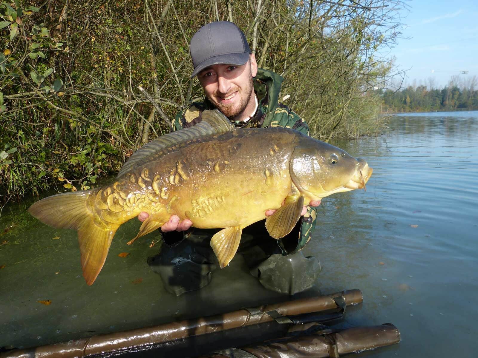 Tortelini-und-Bachkresse-020 Angler hält stolz einen großen Karpfen in der Hand, der mit hochwertigem Angelgerät am See gefangen wurde.