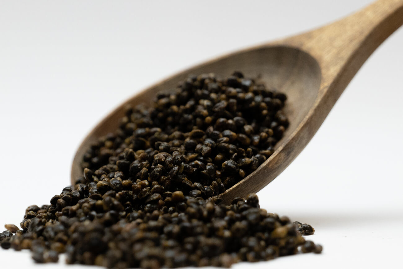 Karpfen Futterhanf - 3 Liter Sessionpack - Widerveschließbar Ein mit dunklen Hanfsamen gefüllter Holzlöffel, ein beliebter Köder zum Karpfenangeln für Spod-Mischungen.
