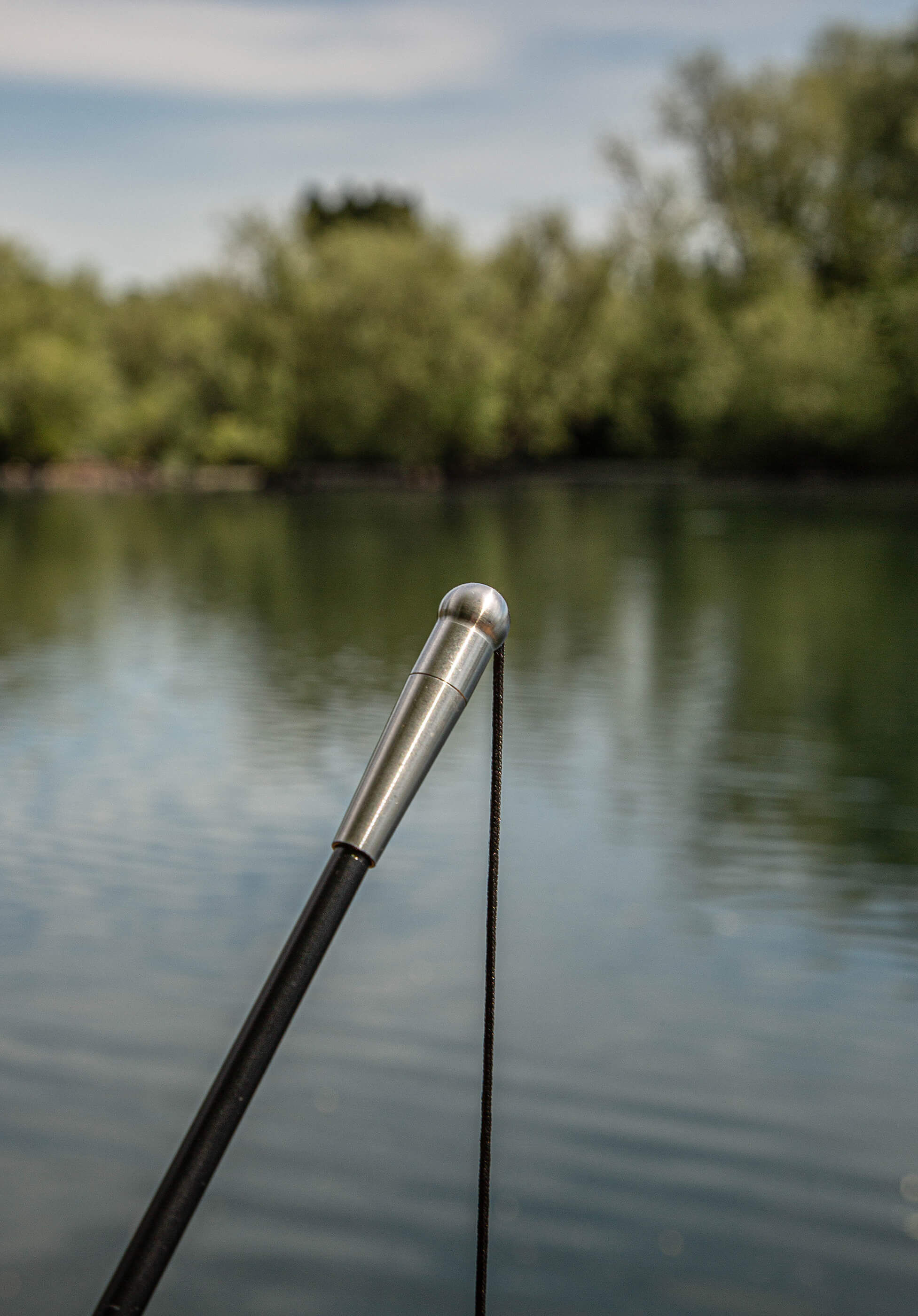 Primo piano di una canna da pesca pronta per la pesca alla carpa in un lago tranquillo.