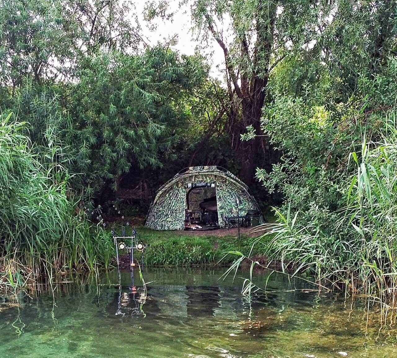 Kaufberater für Angelliege und Schlafsack Ein getarntes Angelzelt am Wasser, ideal für Karpfenangler, die Komfort suchen.