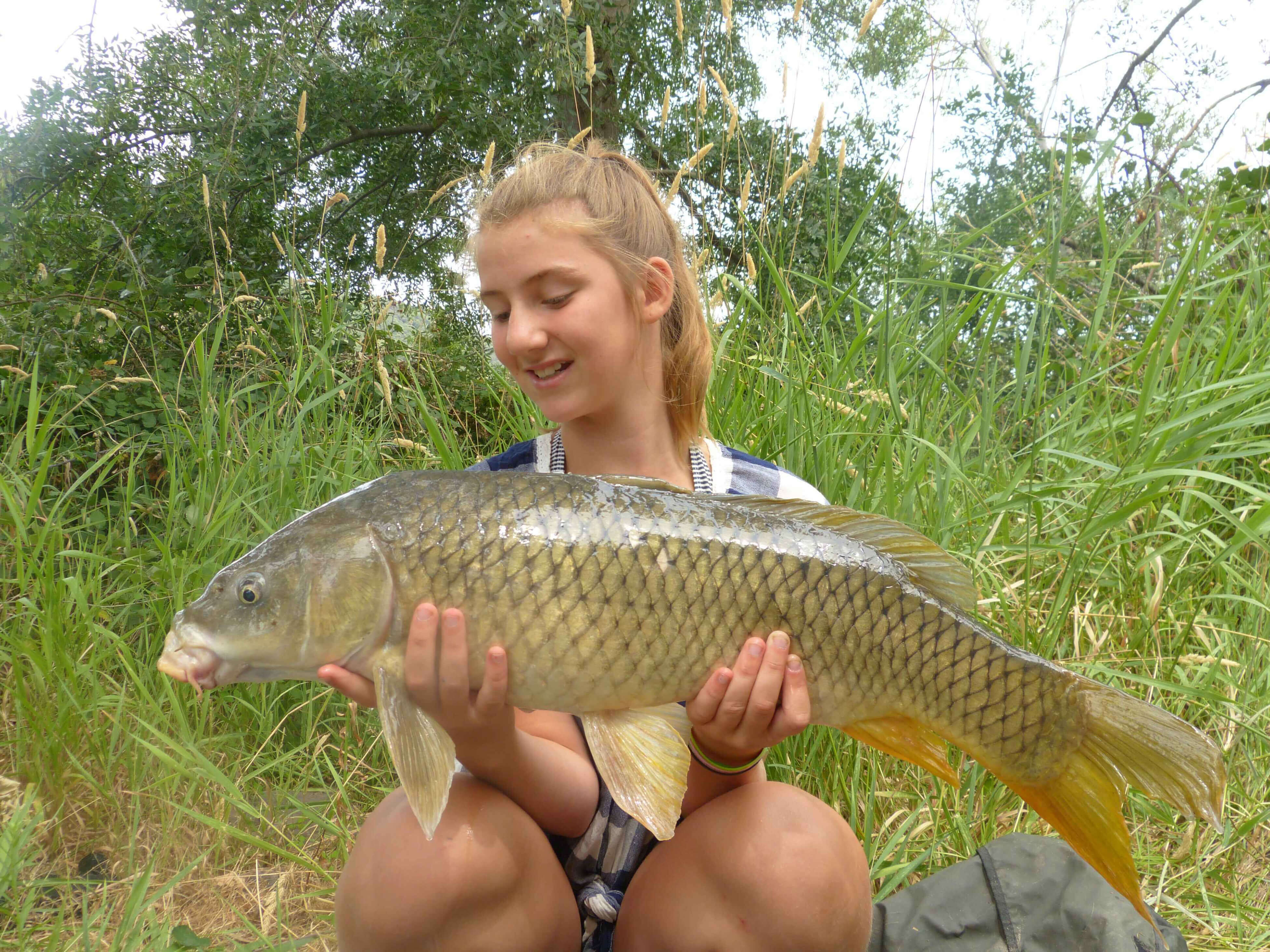 karpfenangeln_frankreich_248 Junger Angler hält stolz einen großen Karpfen in der Hand, der während eines Angelausflugs in der Natur gefangen wurde.