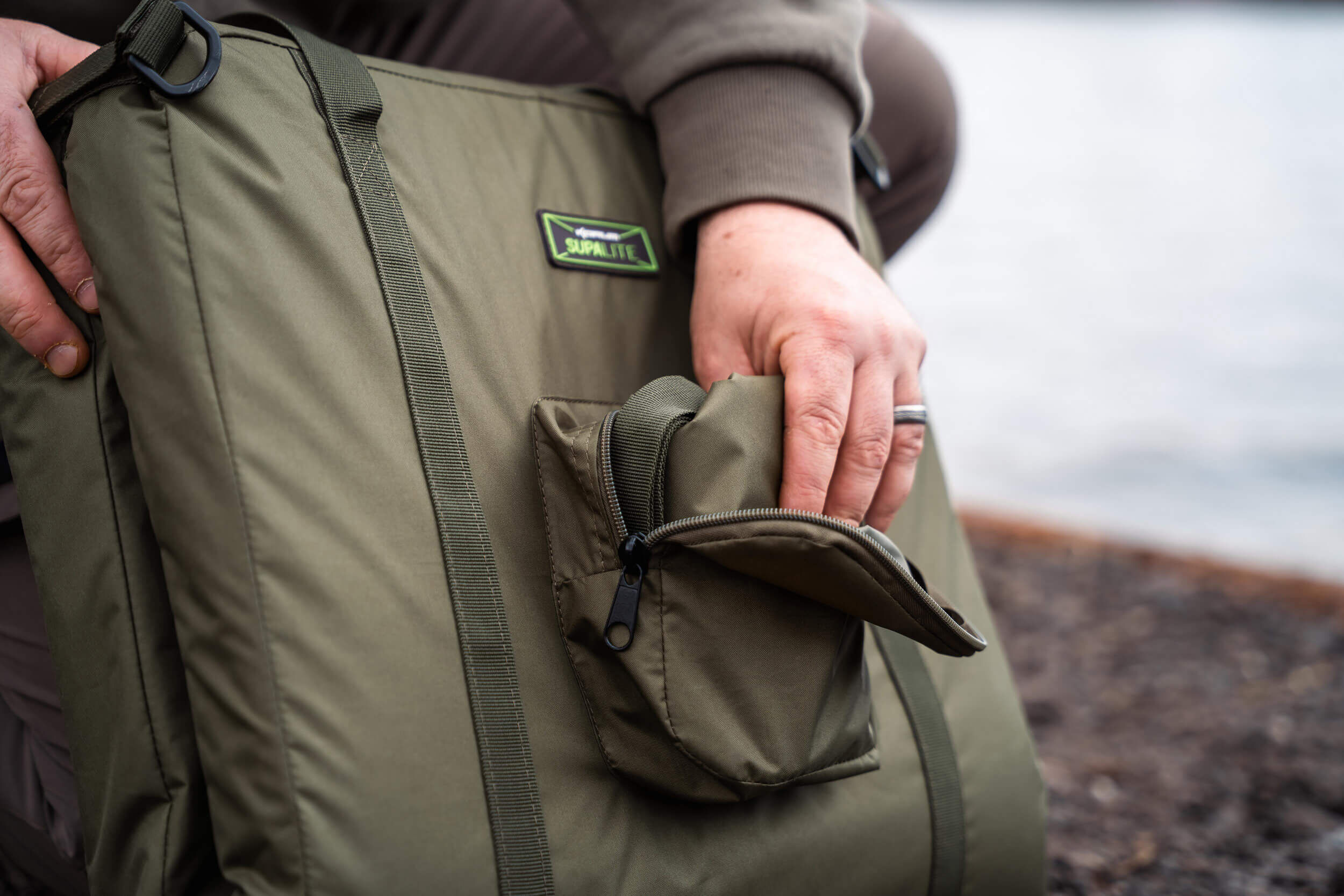 Ein Fischer, der sein Angelgerät in einer robusten, geräumigen Angeltasche am Wasser organisiert.