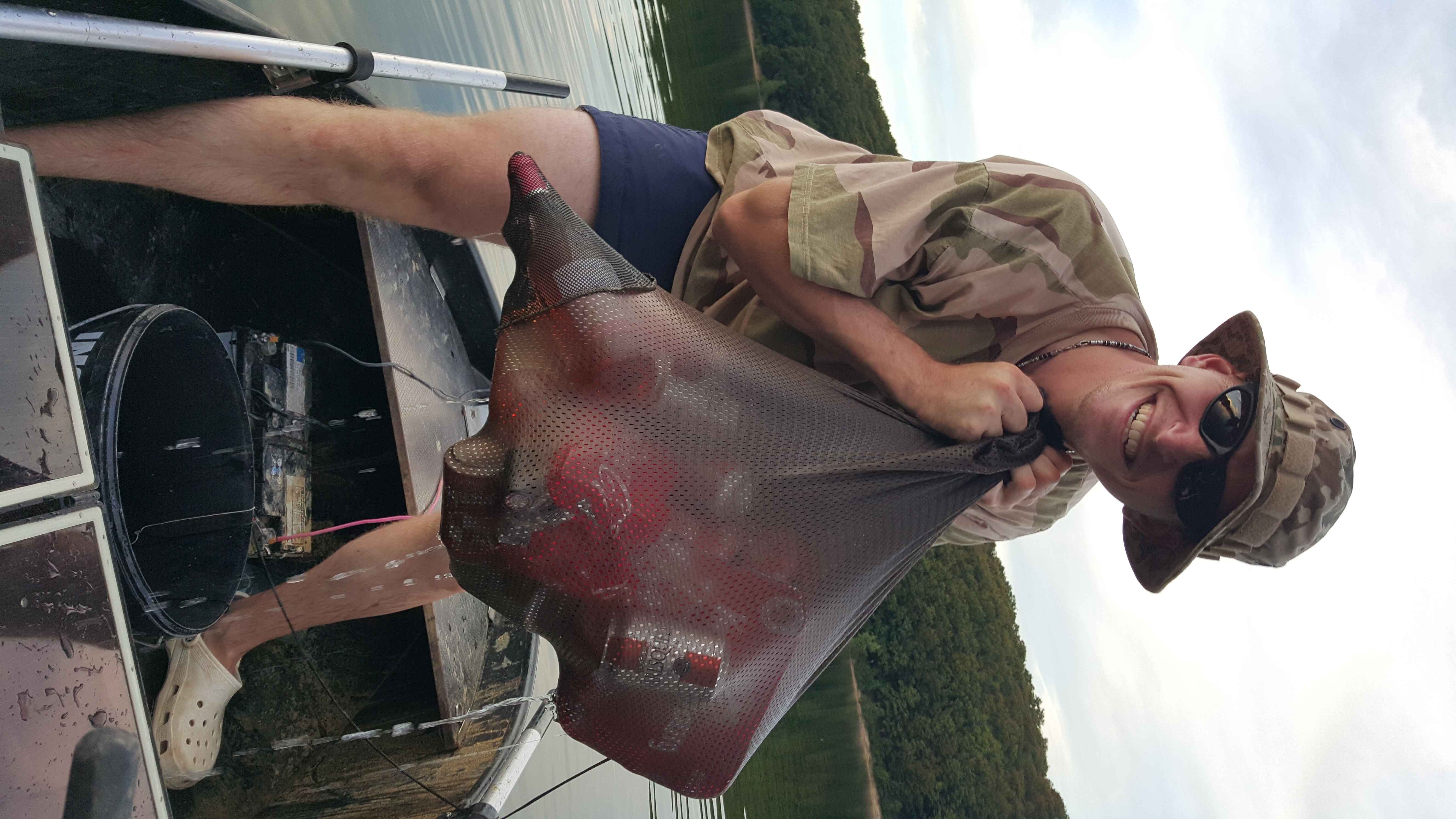 030 Angler zeigt stolz einen Fang in einem Netzbeutel, während er vom Boot aus fischt.
