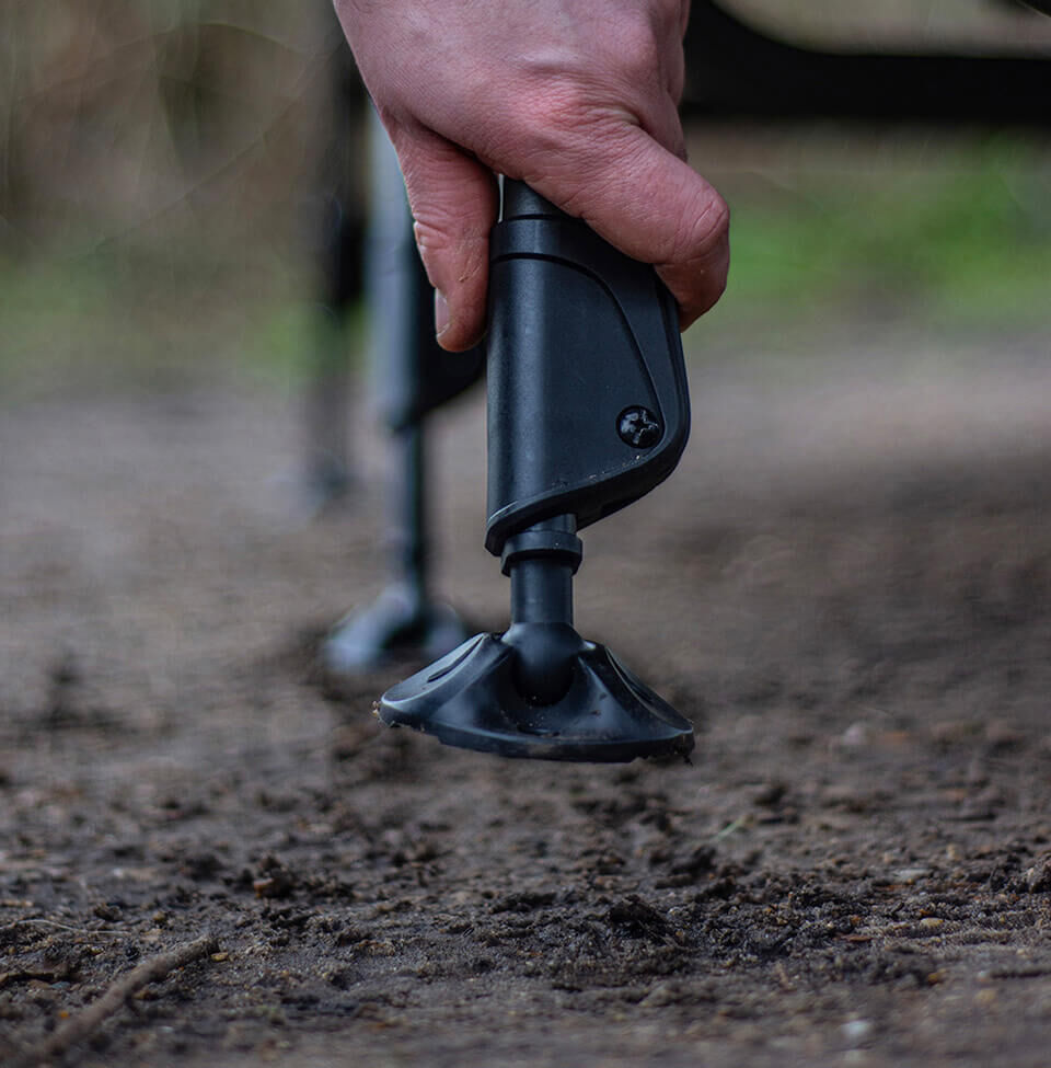 Een visser die de moddervoet van een stretcherpoot voor karpervissen aanpast voor stabiliteit op zachte grond.