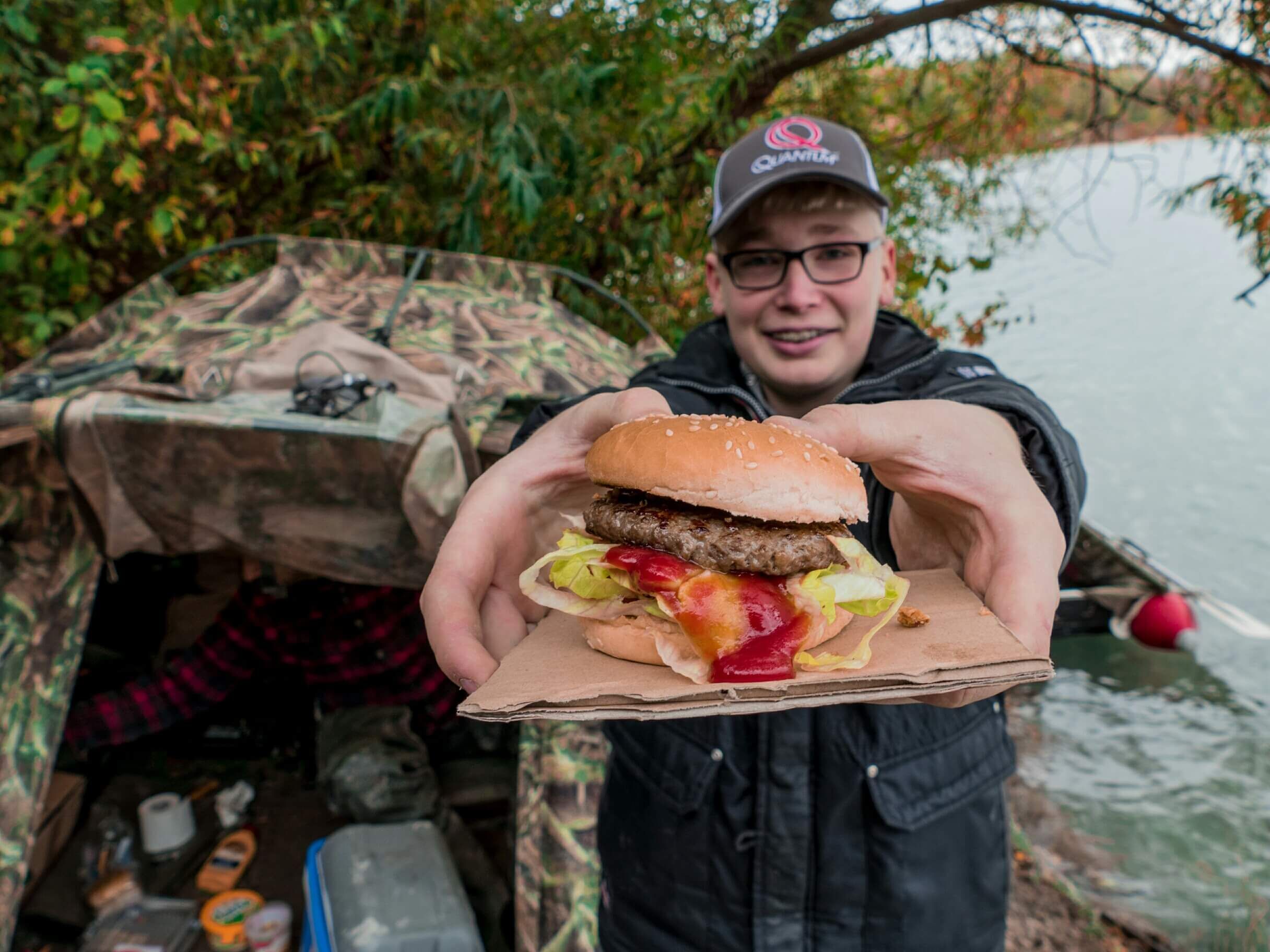 bivvy-hecht Ein junger Angler genießt einen köstlichen Burger beim Angeln am Wasser.