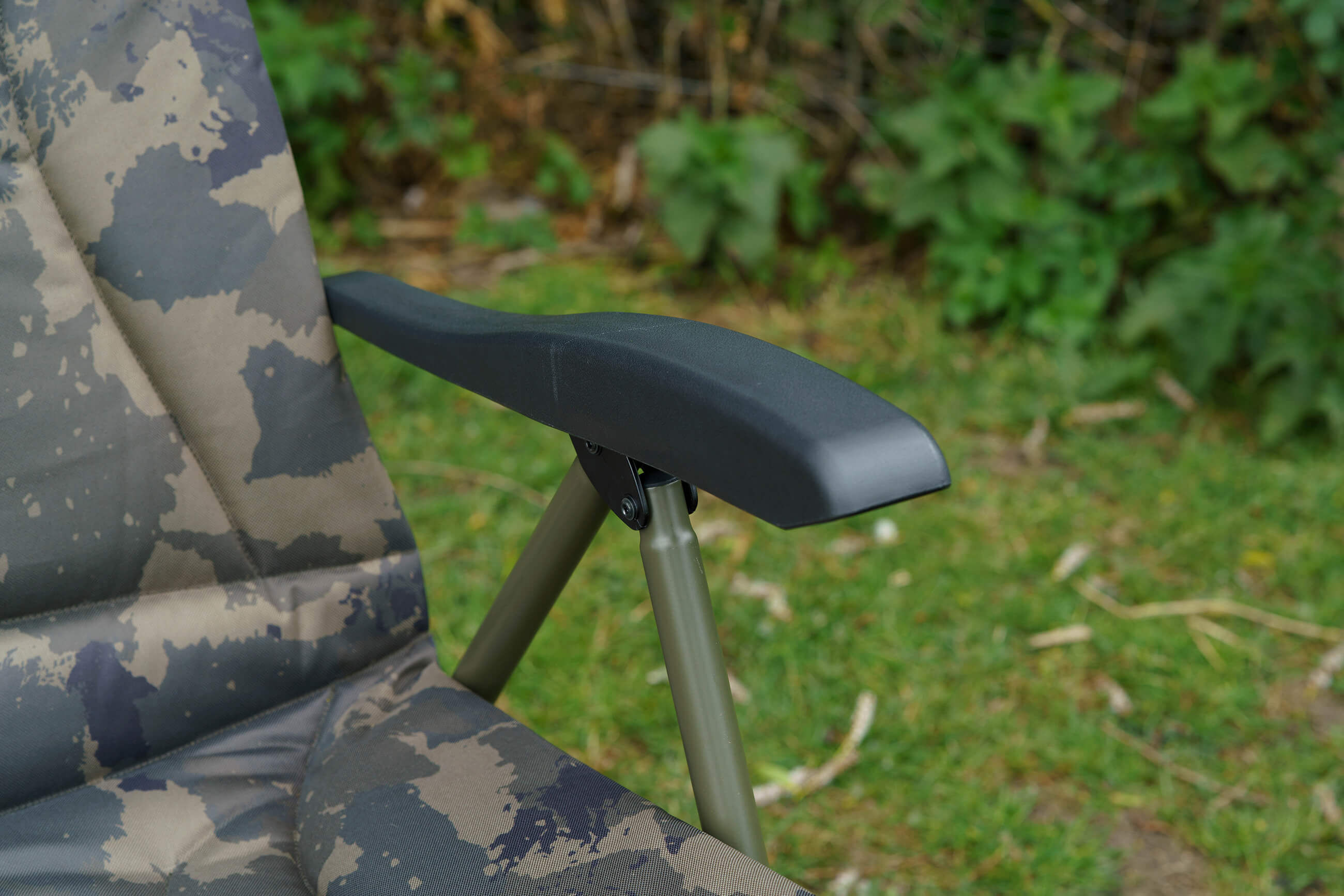 Close-up van een comfortabele karpervisstoel met camouflagestof en een stevige zwarte armleuning.