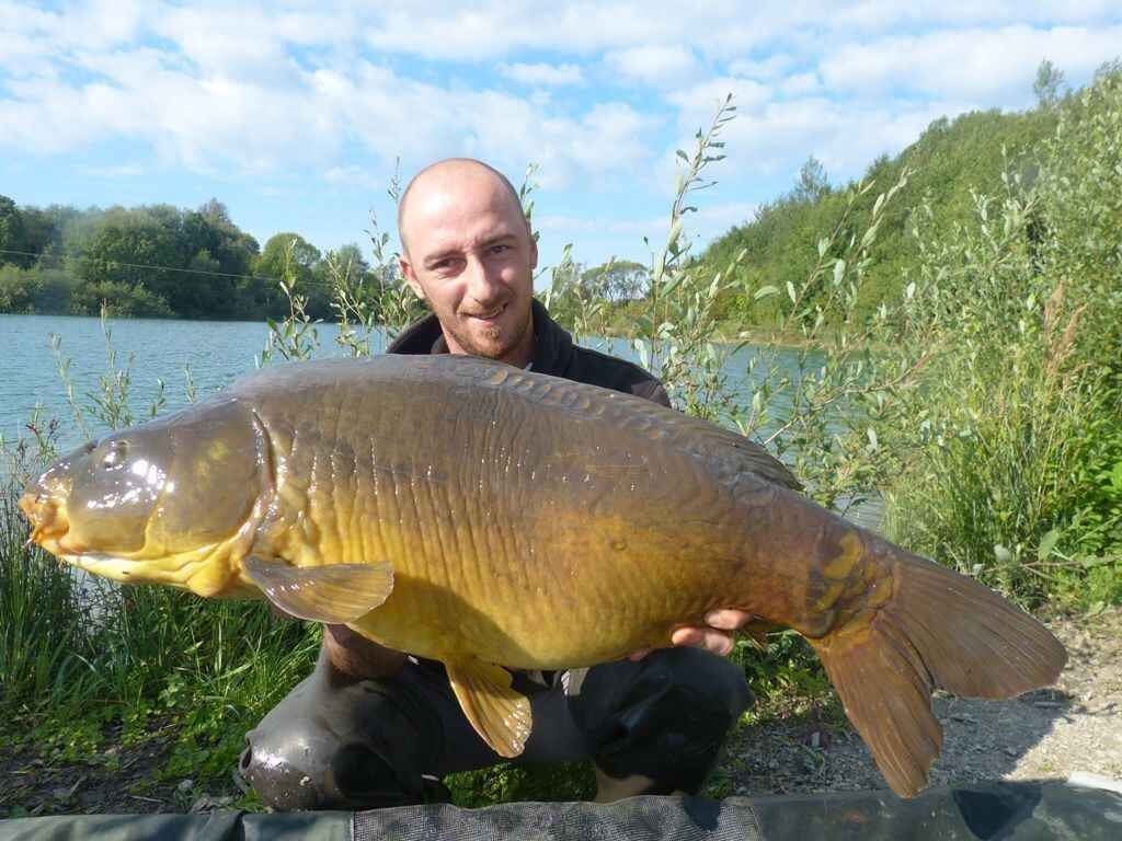 Message in a Bottle - Ostwind & Karpfenangeln Angler hält stolz einen großen Karpfen in der Hand, der mit hochwertigem Angelgerät am See gefangen wurde.