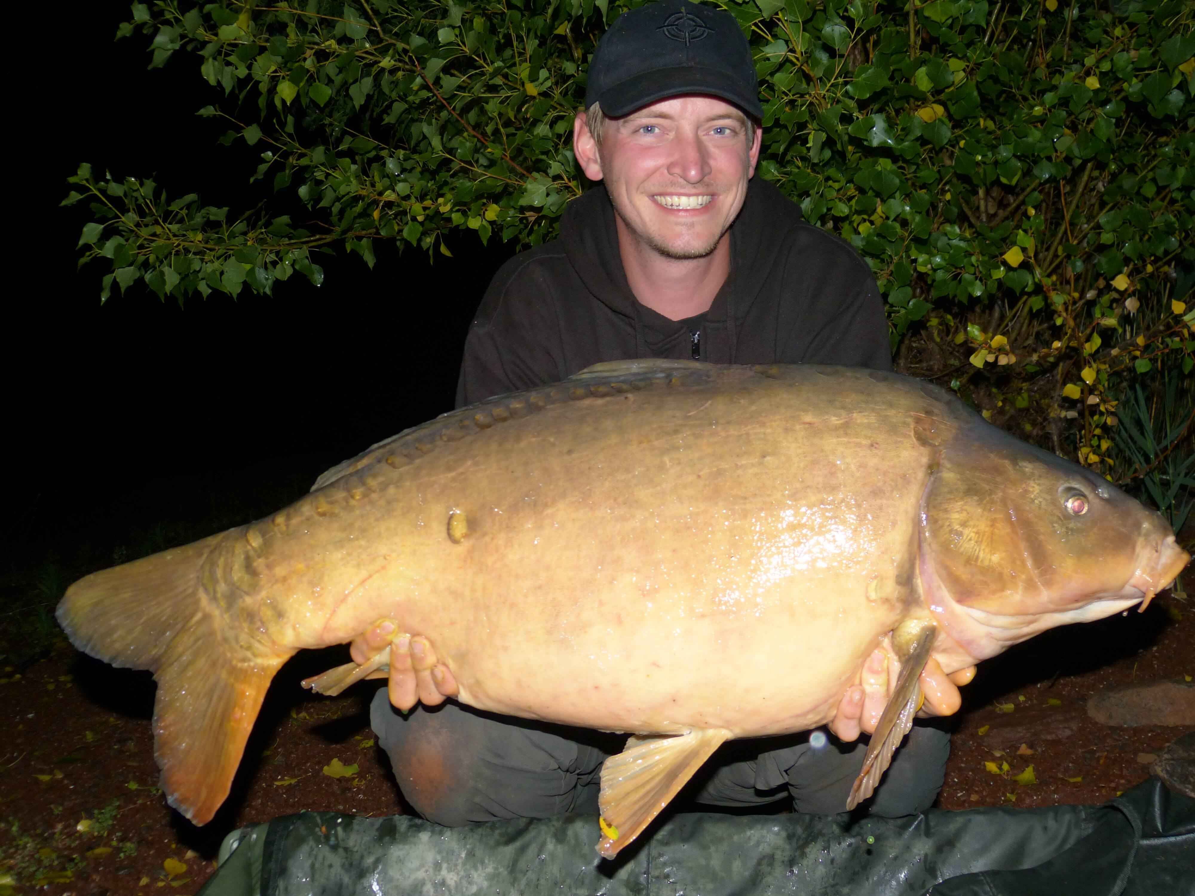 Frankreichtour-mit-Jan-348 Angler hält stolz einen großen Karpfen in der Hand, der nachts gefangen wurde, und präsentiert erfolgreiche Angelausrüstung.