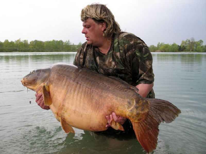 Vorfachmaterial-KRYSTON-Super-Nova-verschiedene-Staerken_b2-png Angler hält stolz einen großen Karpfen in der Hand, der in einer ruhigen Seeumgebung gefangen wurde.