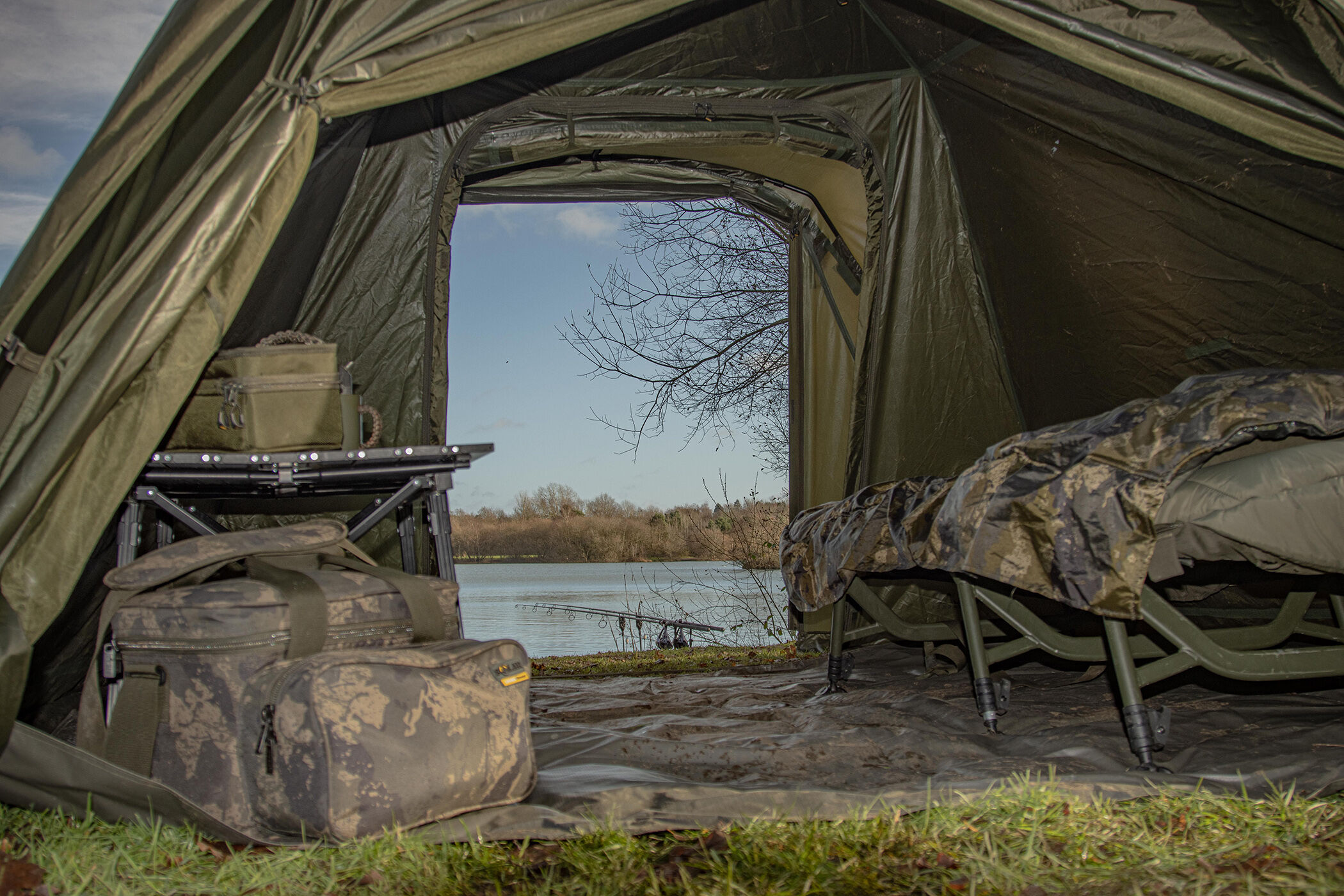 Vista dall'interno di una tenda da pesca, che mostra gli attrezzi essenziali per la pesca alla carpa in acqua.
