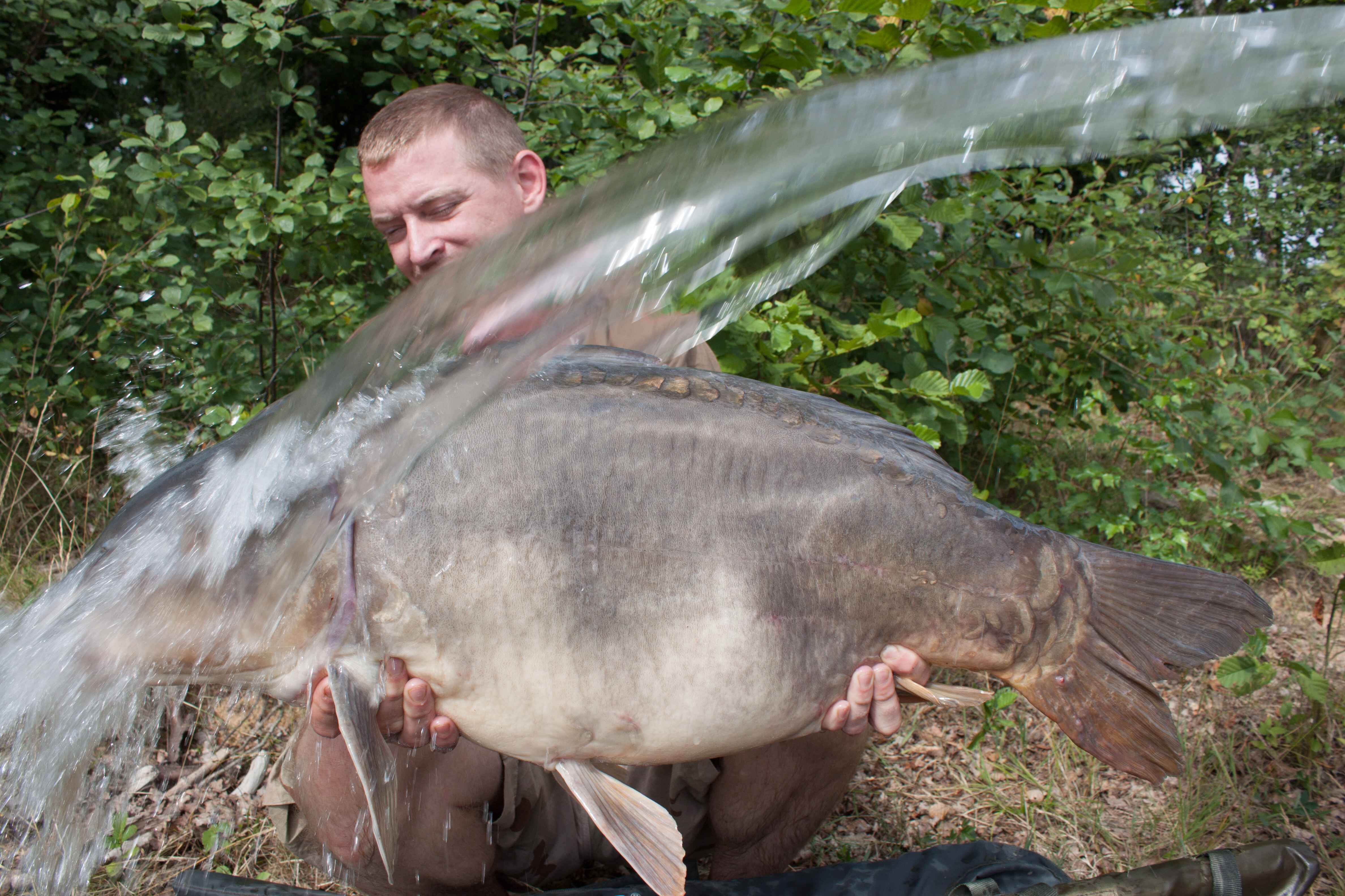 021e Angler hält stolz einen großen Karpfen und präsentiert erfolgreiche Angeltechniken und Ausrüstung.