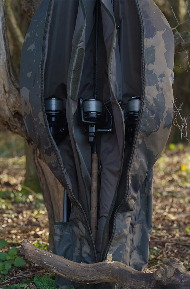 Camo karpervishengeltas met daarin drie hengels met molens, hangend aan een boom.