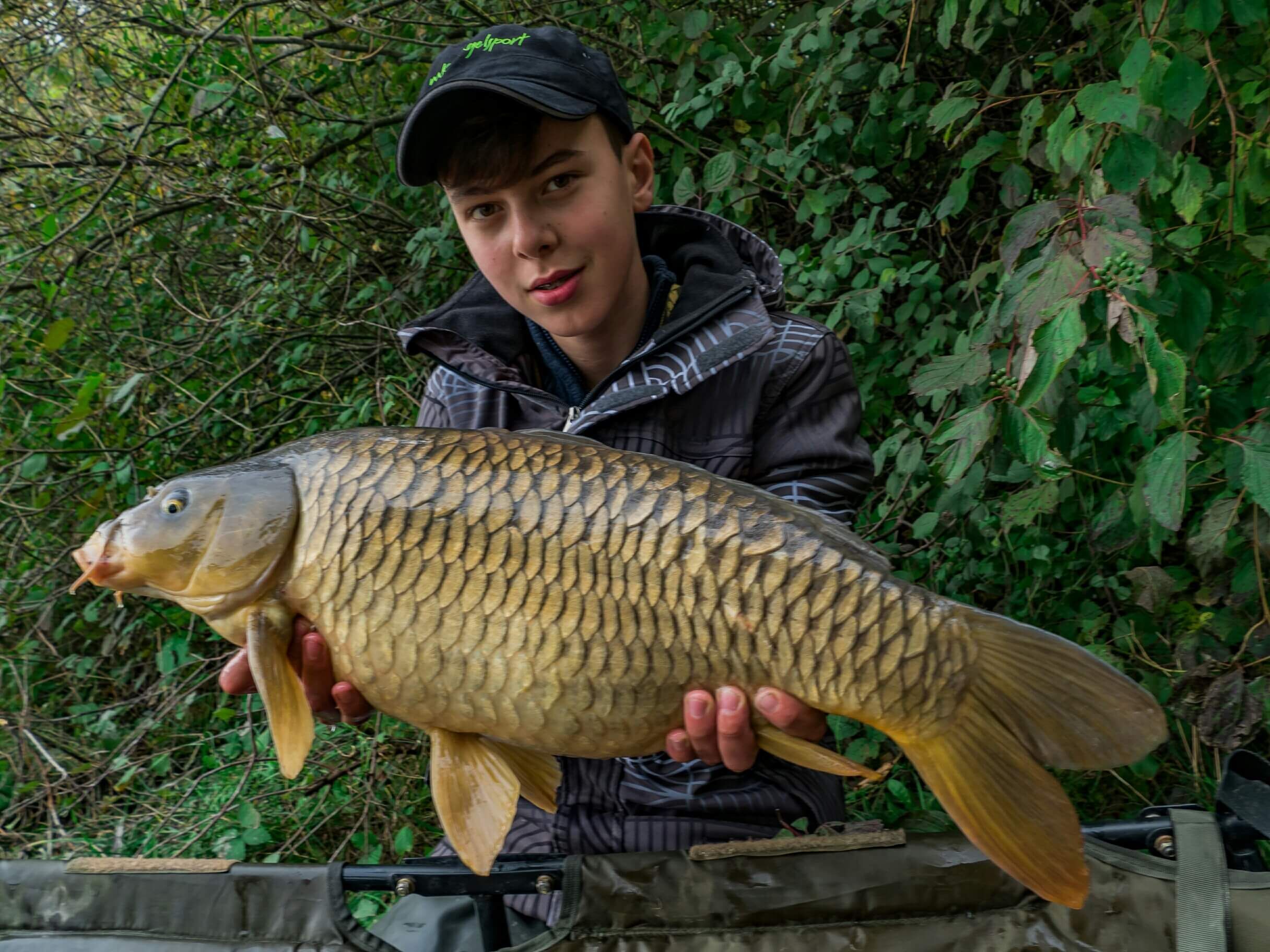 hecht-brolly Junger Angler hält stolz einen großen Karpfen in der Hand, der während eines Angelausflugs in der Natur gefangen wurde.