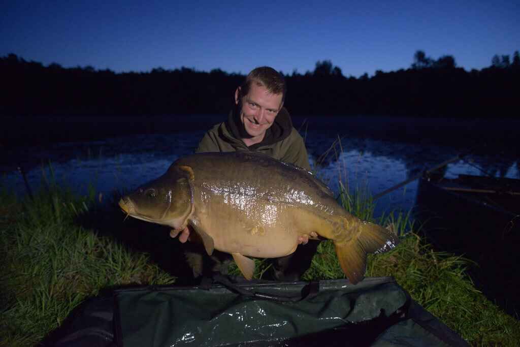 WP5_1593 Angler hält nachts stolz einen großen Karpfen in der Hand und präsentiert erfolgreiche Angelausrüstung.