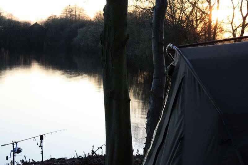 Die Geschichte des Bivvy - Angelzelt Ein friedlicher Angelplatz bei Sonnenuntergang mit Zelt und Angelrute am Wasser.